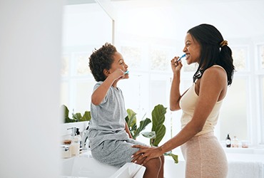 Parent and child smiling while brushing teeth in bathroom