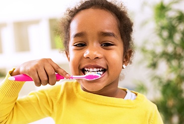 Young girl in yellow shirt smiling while brushing her teeth